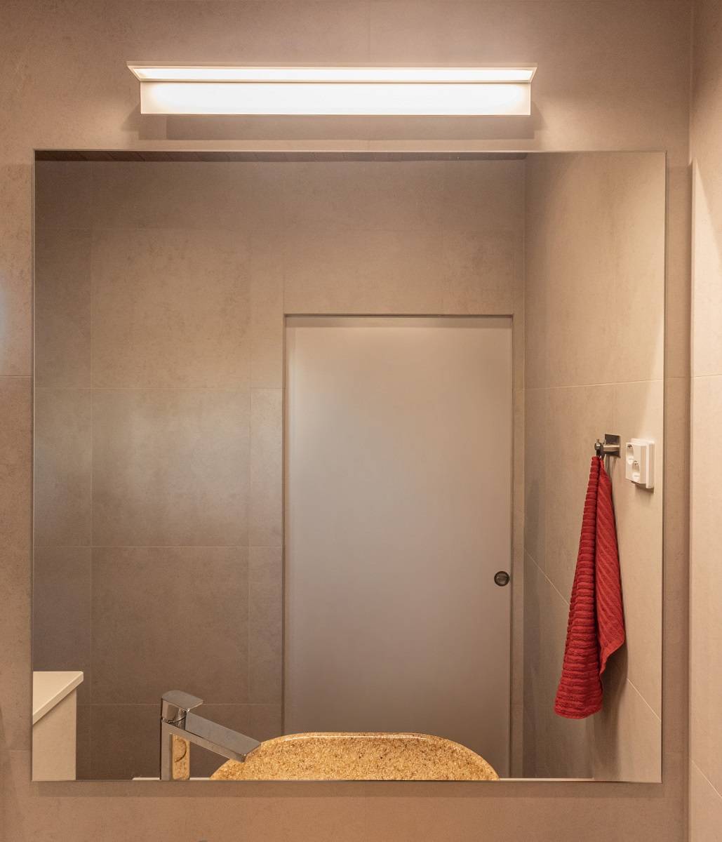En la zona de ducha, encima del lavabo, un aplique BLADE600 blanco con bordes de aluminio proporciona una iluminación uniforme. La luz tiene una temperatura de color cálida de 3.000 Kelvin.